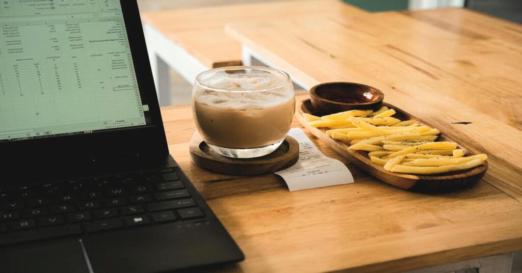 Laptop on coffee shop table showing budget spreadsheet cafe view