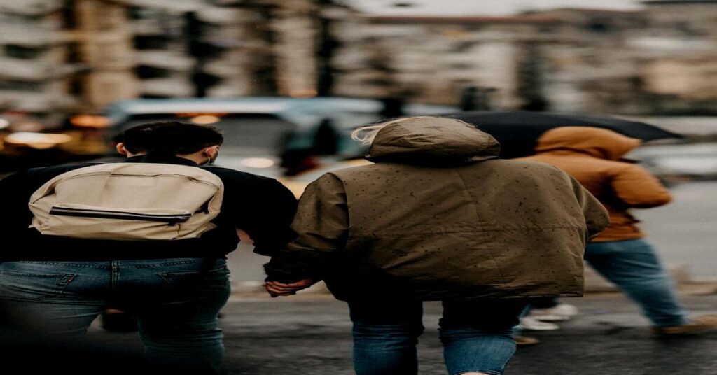Person from behind wearing sleek secure minimalist grey backpack walking on city street crowd blurred