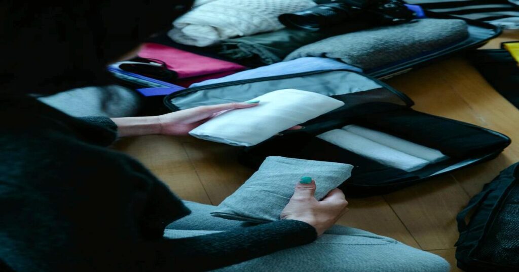 Person packing travel clothes into suitcase top view