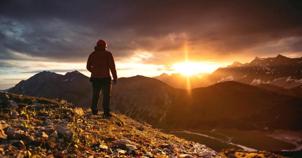 Hidden solo travel deals backpacker standing on scenic mountain peak lookout