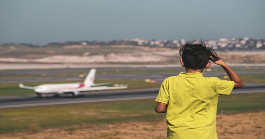 Solo traveler using phone at airport terminal watching airplane takeoffs