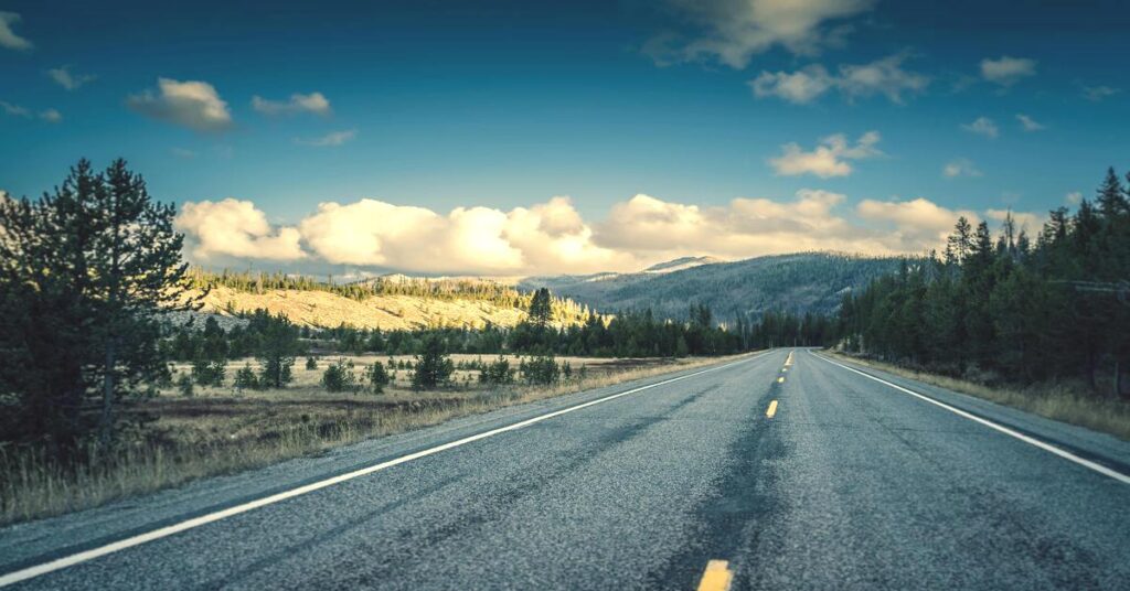 Best Solo Road Trips in the USA featuring an open, sweeping highway winding through magnificent sunny mountains