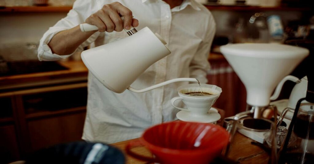 Hands pouring hot water from a travel kettle inside a cozy hostel dorm room setting